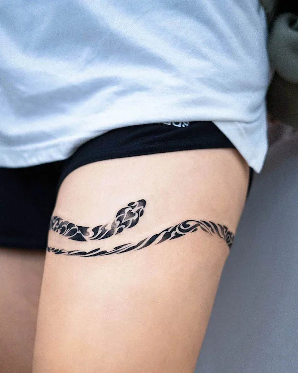 Snake thigh band tattoo, by @e.nal_.tattoo, encircling the thigh with protective symbolism