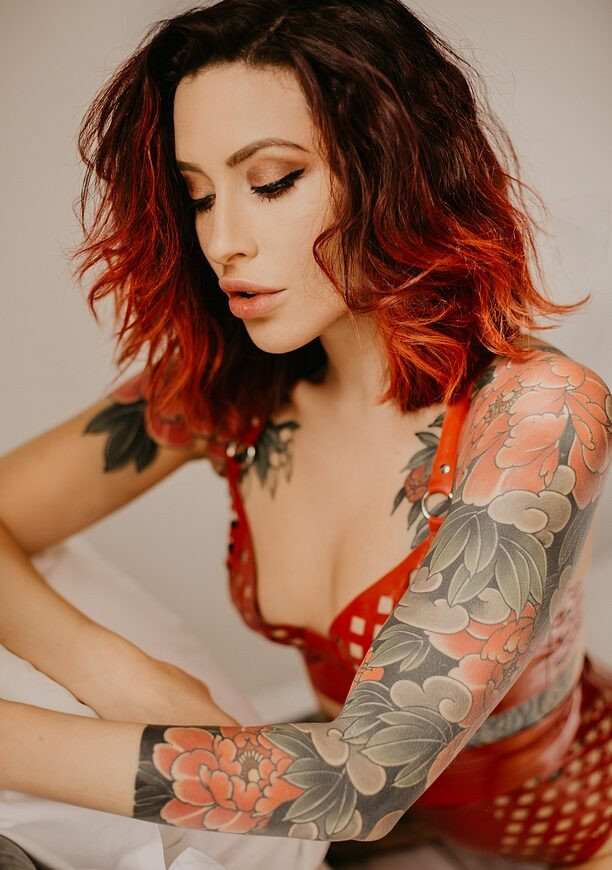 Rodrigo Souto's vibrant peony tattoo on Adreena Angela's shoulder, captured in a dynamic shot by Adam Robertson, showcases the artist's mastery in floral tattoo artistry