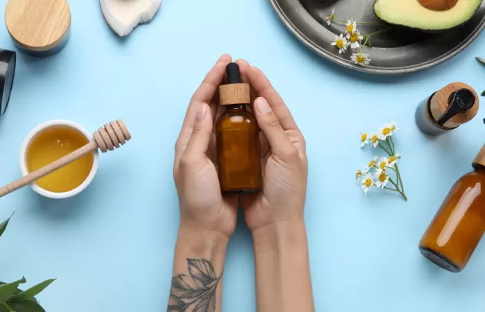 Close-up of tattooed hands holding a bottle of vitamin E oil