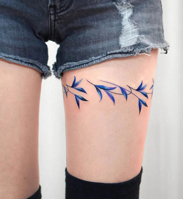 Thigh band tattoo with blue leaves encircling the thigh, by @eden_tattoo_, creating a serene and natural adornment